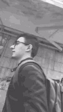 a man wearing glasses and a backpack is standing in front of a building in a black and white photo .