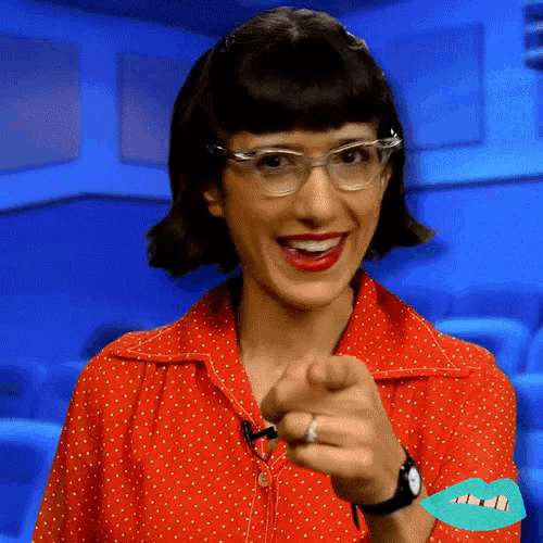 a woman wearing glasses and a red shirt pointing at the camera