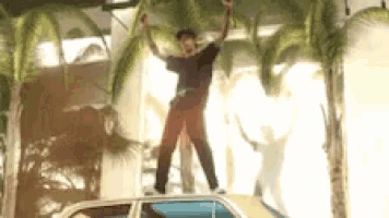 a man is standing on top of a car with his hands in the air .