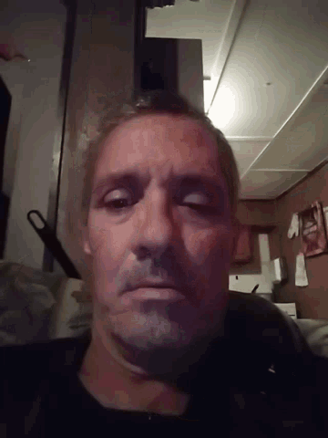 a man with black paint on his face looks at the camera in a dark room