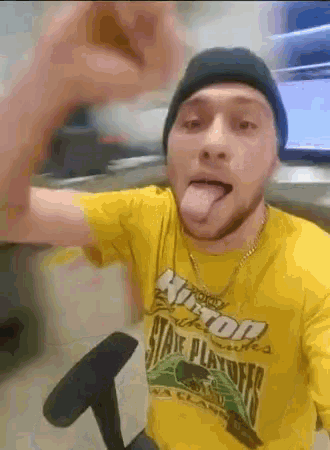 a man wearing a yellow shirt with the word nikon on it is sticking his tongue out