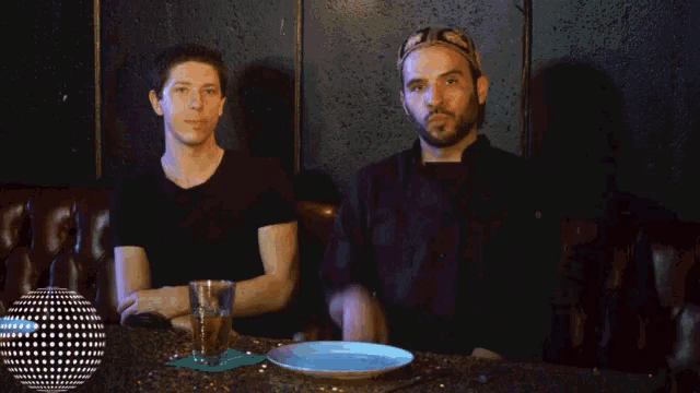two men sitting at a table with a plate of food