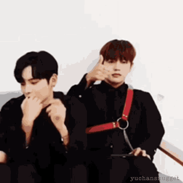 two men are sitting next to each other on a couch and one of them is wearing a red harness .