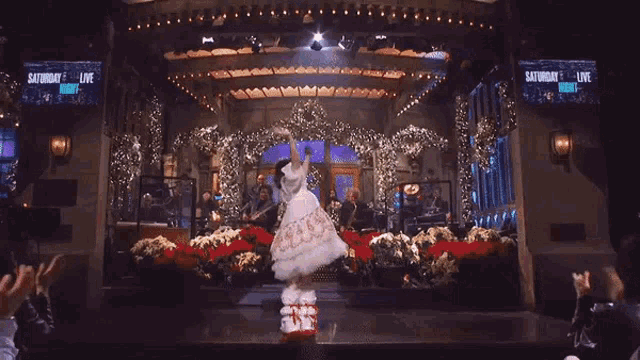 a girl in a white dress is dancing on a stage in front of a saturday night live screen .