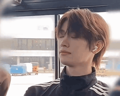 a young man is sitting in a bus with his eyes closed and wearing ear buds .