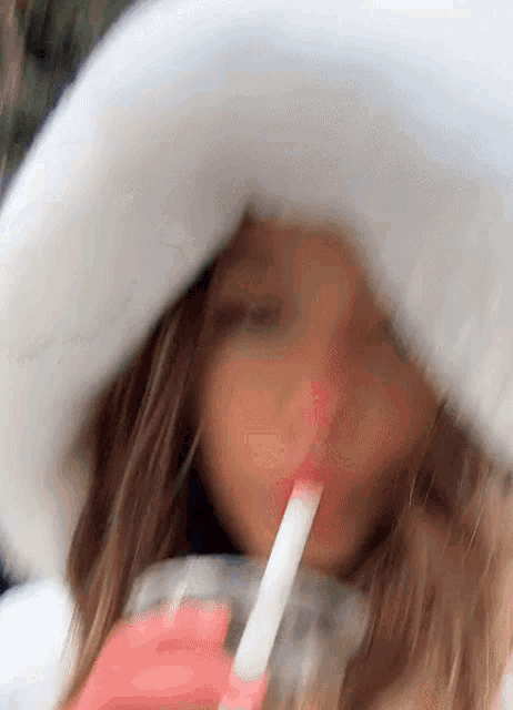 a woman wearing a white hat drinking through a pink straw