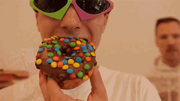 a man wearing sunglasses is eating a chocolate donut with m & m 's