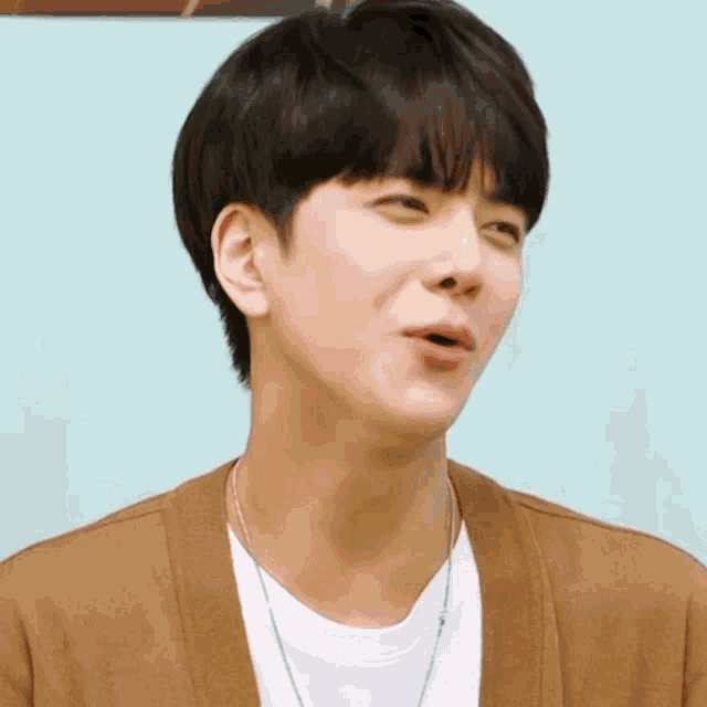 a young man wearing a brown cardigan and a white shirt making a funny face