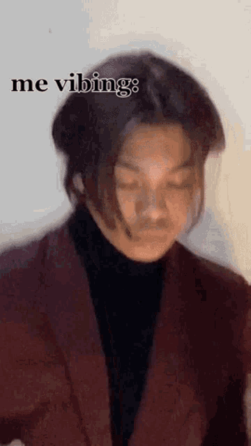 a young man in a suit and turtleneck is making a funny face with his eyes closed .
