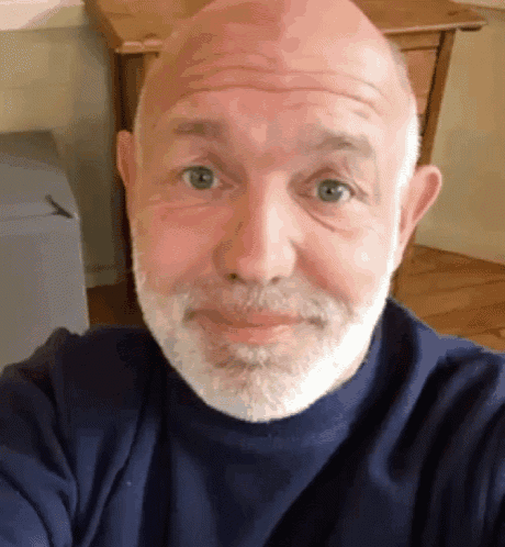 a bald man with a beard and a blue shirt is taking a selfie .