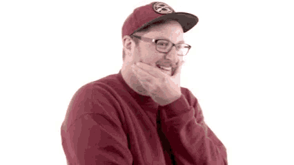 a man wearing glasses and a red sweater is covering his mouth with his hand .