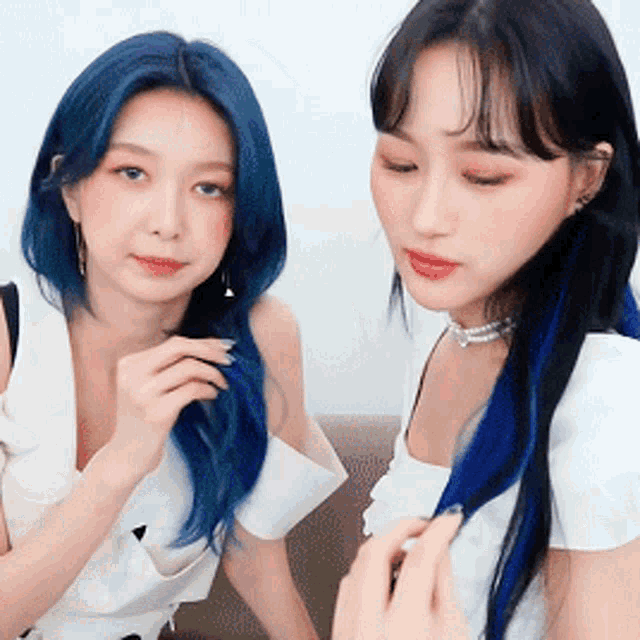 two women with blue hair and black hair are sitting next to each other on a couch .