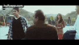 a man in a plaid shirt is talking to a man in a brown coat .