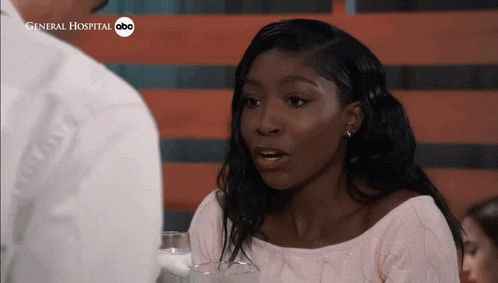 a woman sitting at a table with a glass of water and a general hospital abc logo