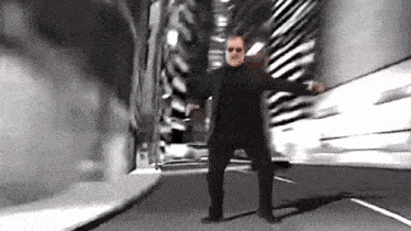 a man in a suit and sunglasses is dancing on a street in a tunnel .