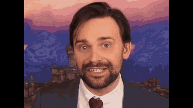 a man with a beard wearing a suit and tie is smiling