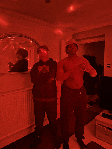 a shirtless man stands next to another shirtless man in a living room