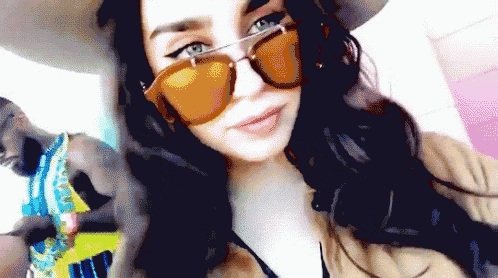 a woman wearing a hat and sunglasses is taking a selfie