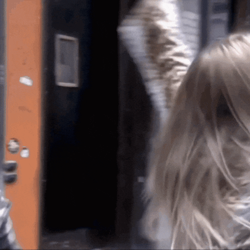 a woman with long blonde hair is standing in front of a door