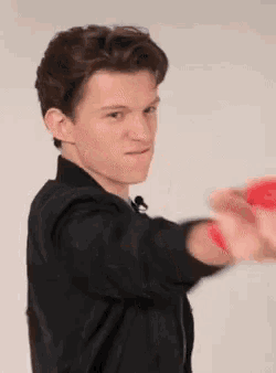 a young man in a black jacket is holding a red object in his hand and making a funny face .