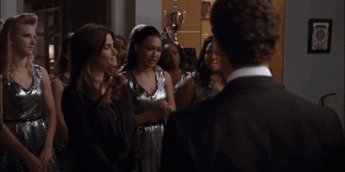 a man in a suit stands in front of a group of women wearing silver dresses
