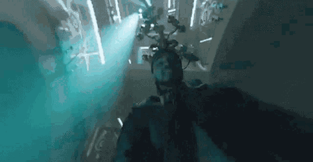 a man in a hooded jacket is standing in a room with a lot of lights on the ceiling .