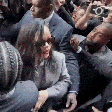 a woman in sunglasses is being escorted by a man in a suit in a crowd .