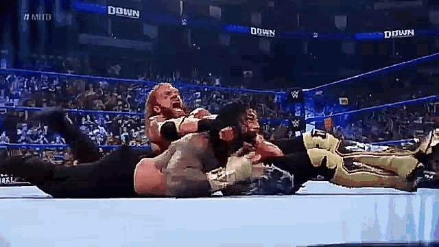 two men are wrestling in a wrestling ring and one of them is laying on the ground .
