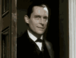 a man in a tuxedo and bow tie is peeking out of a door .