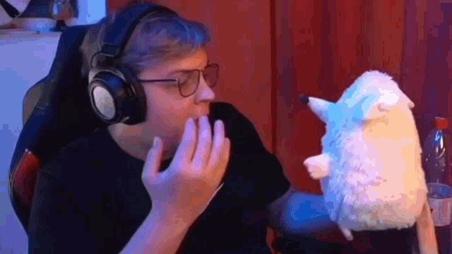 a man wearing headphones and glasses is holding a stuffed animal in his hand .