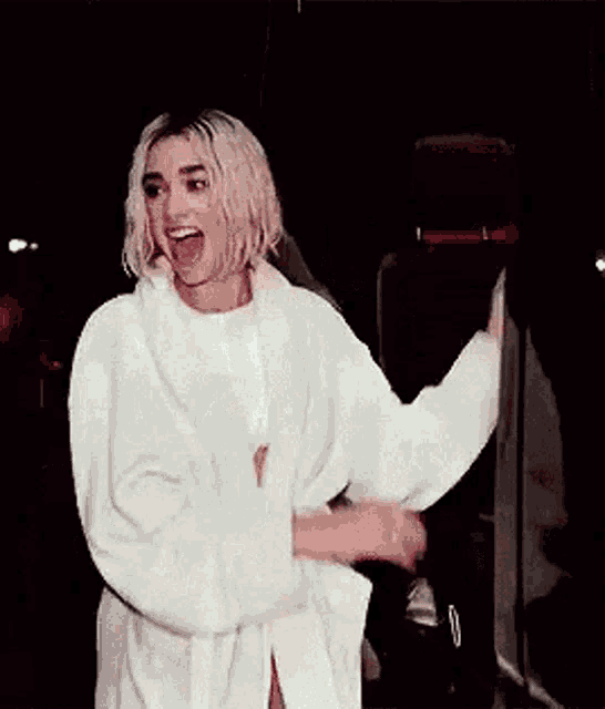 a woman in a white robe is standing in a dark room with her hands folded and smiling .