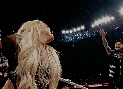 a woman with long blonde hair stands in a wrestling ring with a man in a black shirt that says wwe