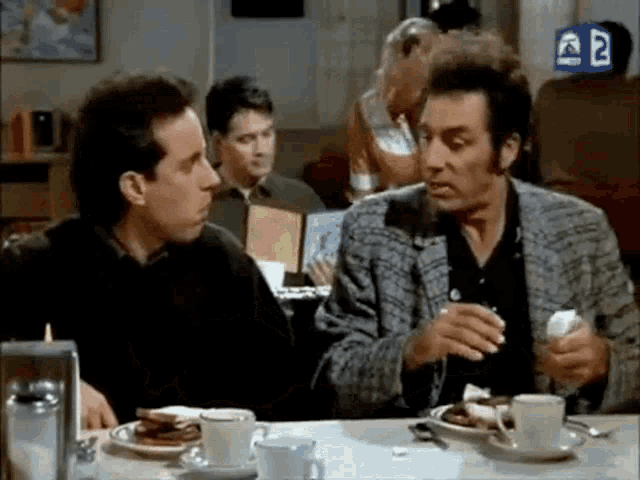 two men are sitting at a table in a restaurant eating food .