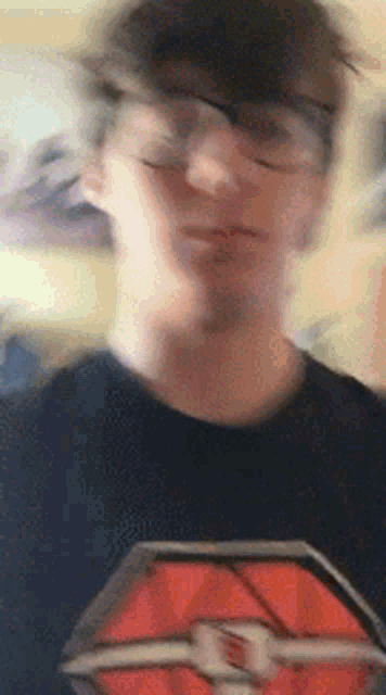 a blurry picture of a young man wearing glasses and a black shirt with a red logo on it .