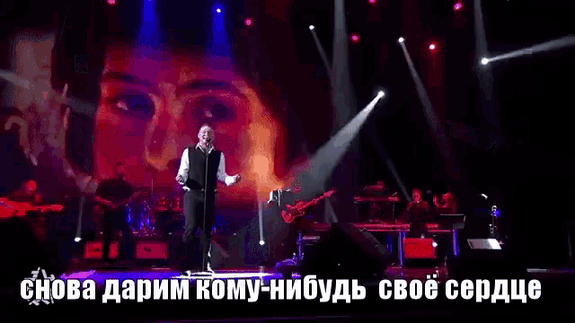 a man singing into a microphone on a stage in front of a large screen