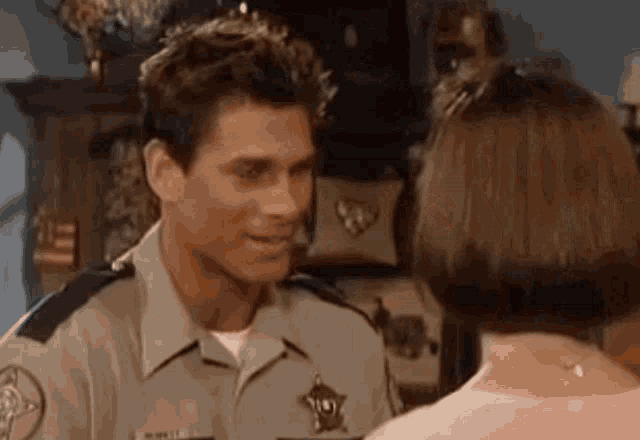 a man in a sheriff 's uniform is talking to a woman in a pink shirt .