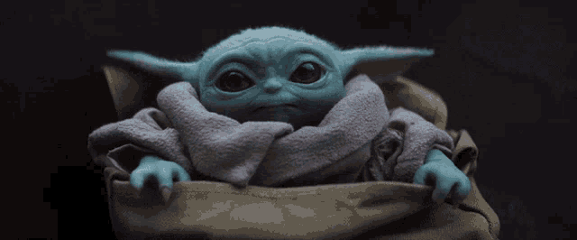 a baby yoda toy is sitting in a bag and looking at the camera