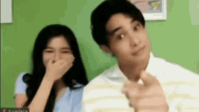 a man and a woman are standing next to each other and laughing . the man is pointing at the camera .
