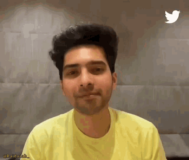a man wearing a yellow t-shirt with a twitter logo in the background