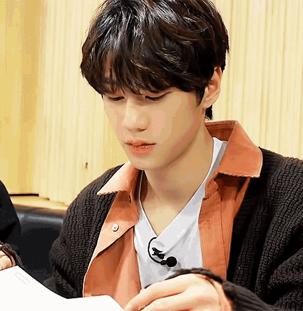 a young man wearing a sweater and a microphone is looking at a piece of paper