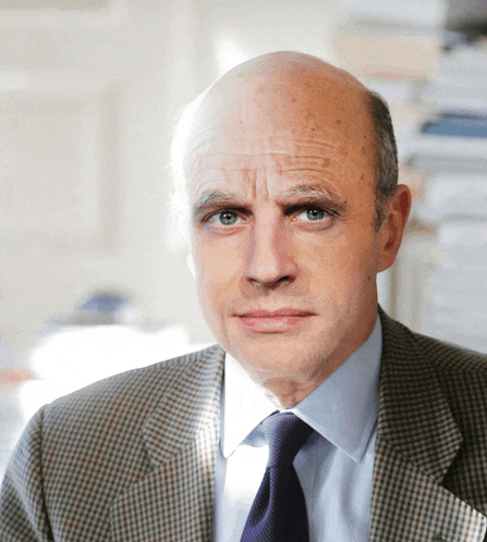 a bald man in a plaid suit and tie looks at the camera