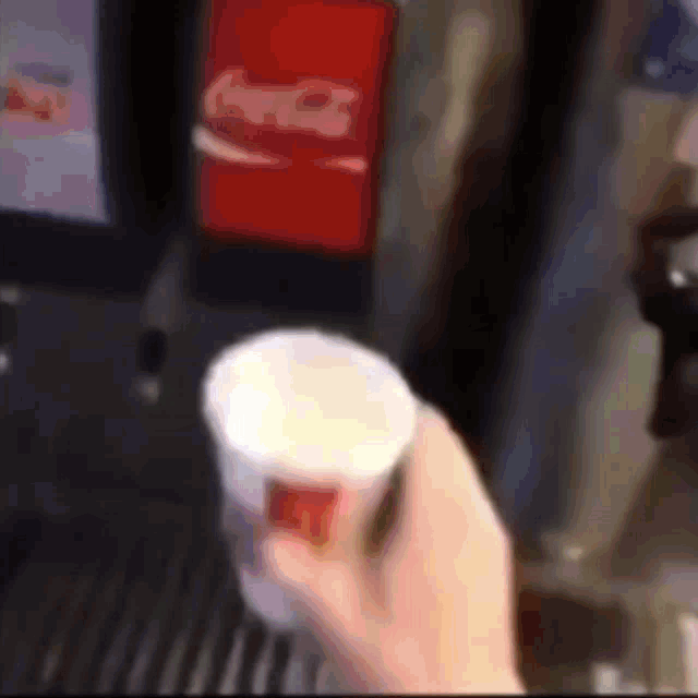 a person is holding a cup of soda in front of a coke machine