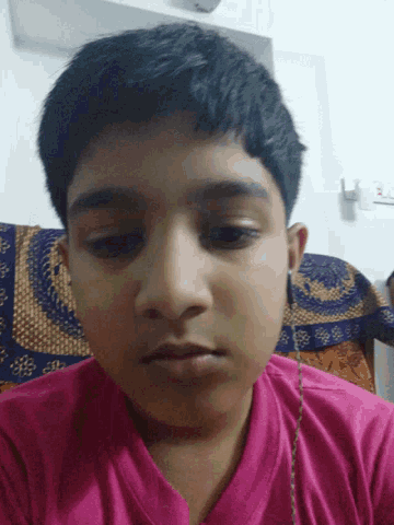 a young boy in a pink shirt looks at the camera with his eyes closed