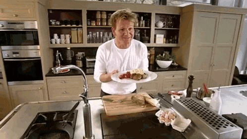 a man in a white shirt is holding a plate of food in a kitchen