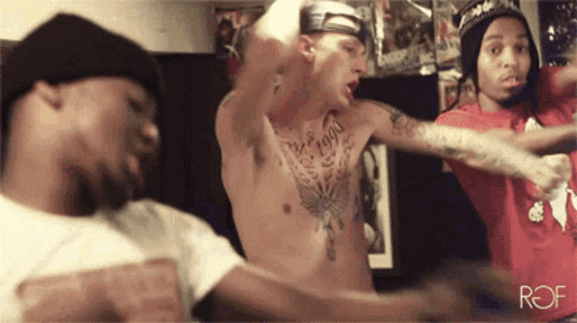 a shirtless man with the year 1990 on his chest is dancing with two other men