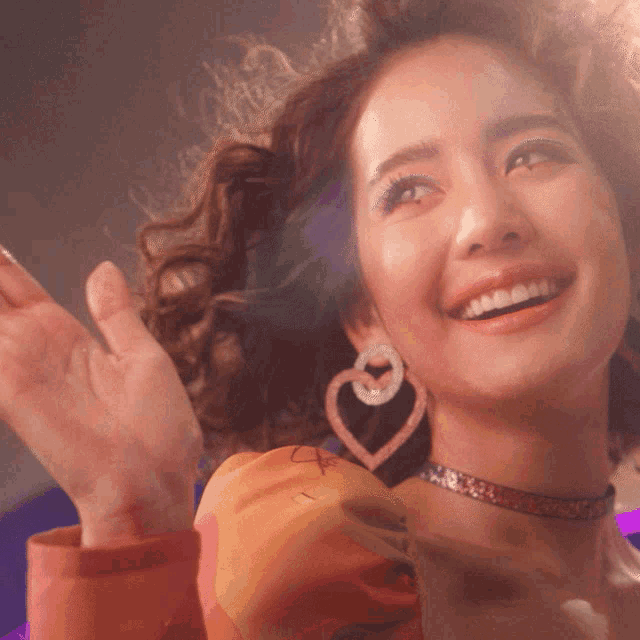 a woman wearing a heart shaped earring and a choker smiles