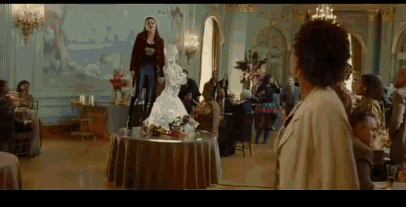 a woman in a red jacket stands in a room with a statue on a table
