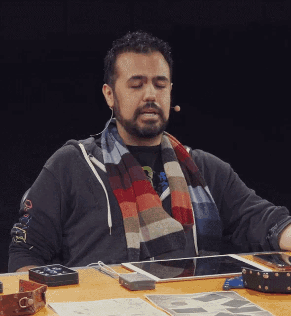 a man with a scarf around his neck is sitting at a table