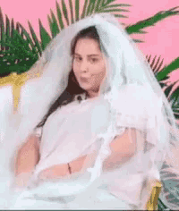 a woman in a wedding dress and veil is sitting on a chair .