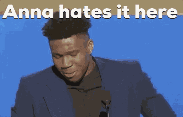 a man in a suit stands in front of a microphone with the words anna hates it here behind him